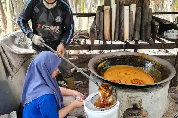 Two farmers at a wok stove, straining freshly boiled sugar into a pail