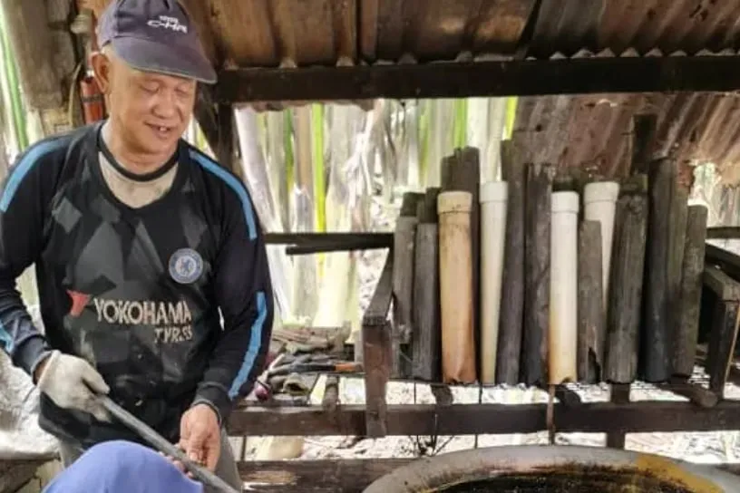 Inside a village hut under a zinc roof: bamboo sap-collection tubes racked in a row, a ladle resting across a wok at the front