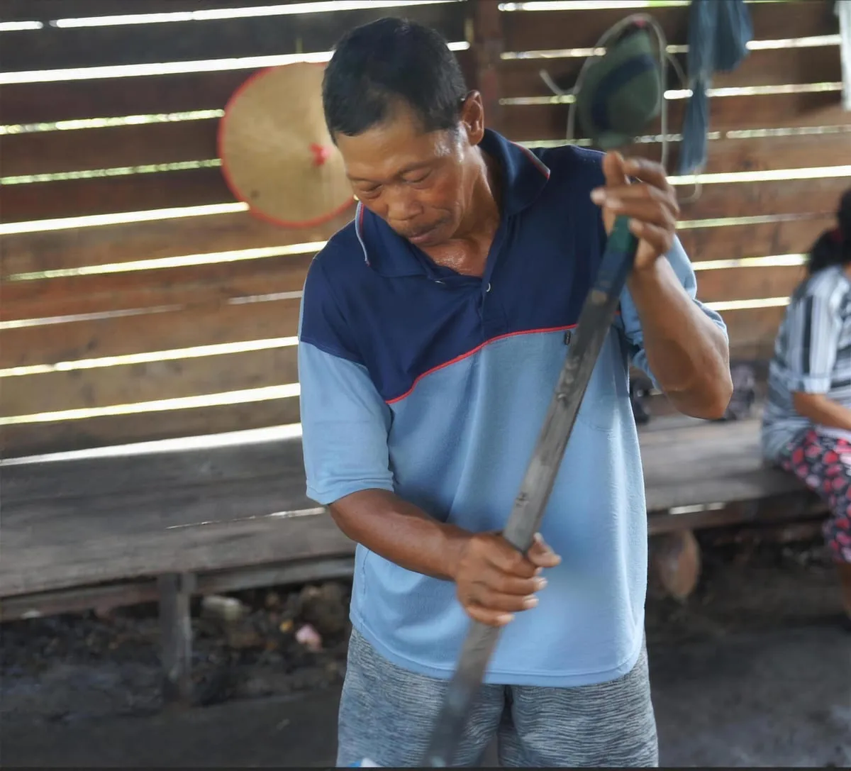 A farmer sharpens his tapping knife in an open-sided wooden shelter.