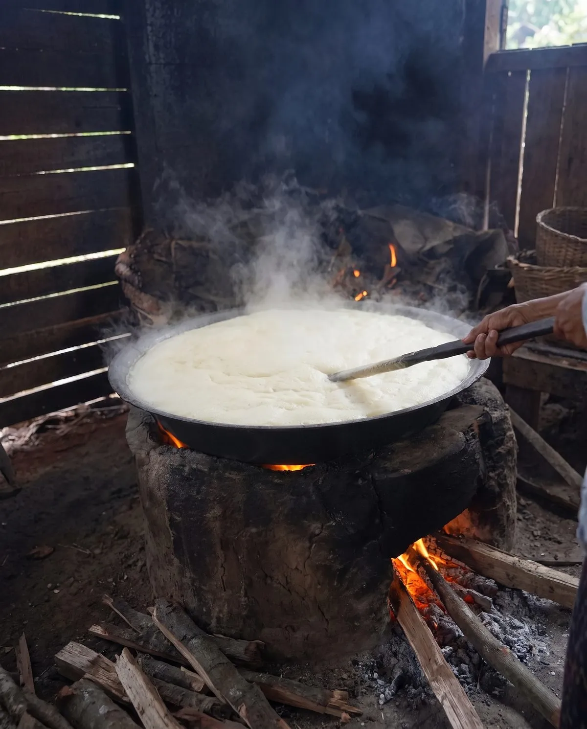 Sap boiling to a pale foam in a wide wok over a wood fire, stirred with a wooden paddle